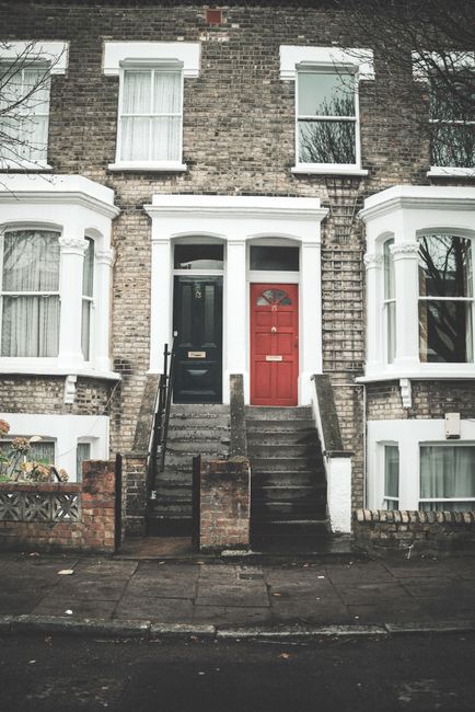 A row of colorful Victorian terrace houses on Rushey Green, with facades painted in pastel shades of blue, pink, and beige. The buildings feature white decorative trim around the windows and doors, an